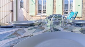 A dining table set with plates, glasses, and cutlery, with a view of a stone building and a gate in the background.