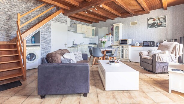 A spacious living area with a high wooden ceiling, a built-in kitchen, and a staircase leading to a laundry room.