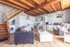 Een ruime woonruimte met een hoog houten plafond, een geïntegreerde keuken en een trap naar een wasruimte.