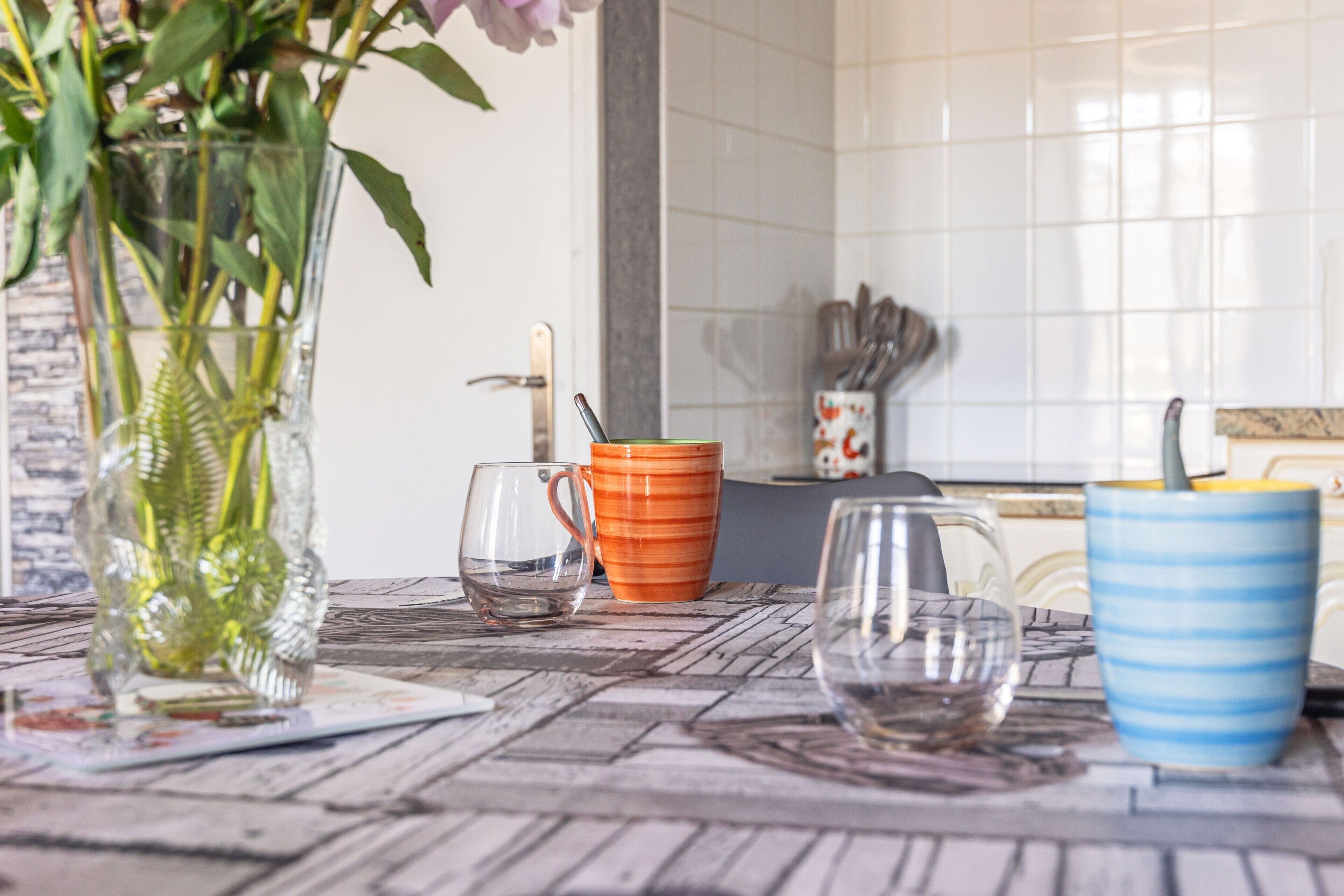 A kitchen counter with a vase, a glass, and two mugs.