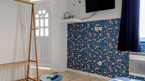 Ein Zimmer mit einer Holzleiter, einem an der Wand montierten Fernseher, einer Wand mit Blumenmuster und einem Fenster mit weißem Rahmen.