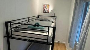 Une chambre avec un lit superposé, un tableau accroché au mur, une porte avec des rideaux et un plancher en bois.