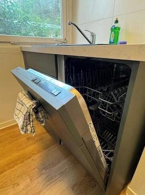 Una cocina compacta con lavavajillas integrado, una ventana con vistas a zonas verdes y una toalla colgada en la puerta.
