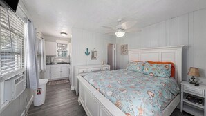 A bedroom with a bed, a nightstand, a ceiling fan, and a view of the kitchen. - Sunset Cottages Suite 1 (Indian Shores)