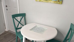A round white table with a fan, two teal chairs, and a beach-themed painting on the wall. - Sunset Cottages Suite 1 (Indian Shores)