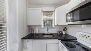 A compact kitchen with white cabinets, a black countertop, a stainless steel sink, a microwave, and an oven. - Sunset Cottages Suite 1 (Indian Shores)