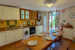 A kitchen with a wooden table set for dining, a washing machine, a microwave, and a sink. - Casa Ilune (Cala Gonone)