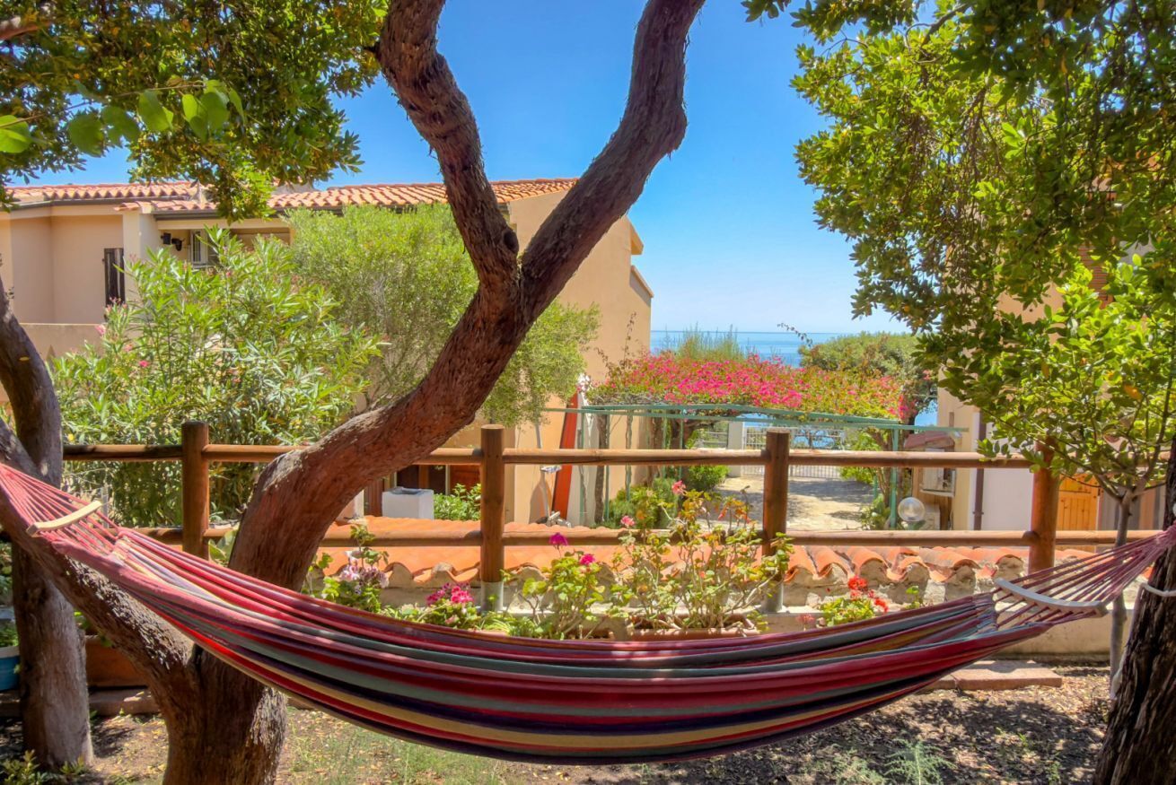 A hammock tied between trees in a garden with a building in the background.