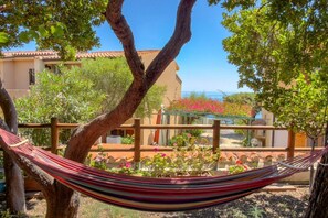 A hammock tied between trees in a garden with a building in the background. - Casa Ilune (Cala Gonone)