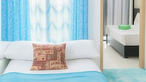Un dormitorio con cama, almohada, cubrecama azul y vista a otra habitación por una puerta abierta.