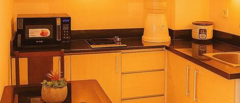 A compact kitchen with wooden cabinets, a microwave, a coffee maker, and a toaster.