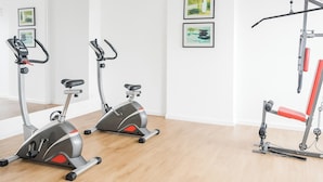 Un gimnasio con dos bicicletas estáticas, un banco rojo y una barra para dominadas.