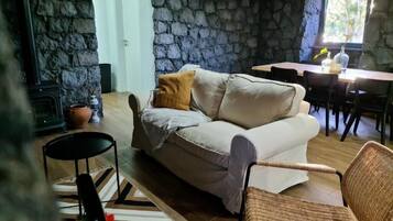 A cozy living area with a stone wall, a sofa, a wicker chair, a dining table, and a fireplace.
