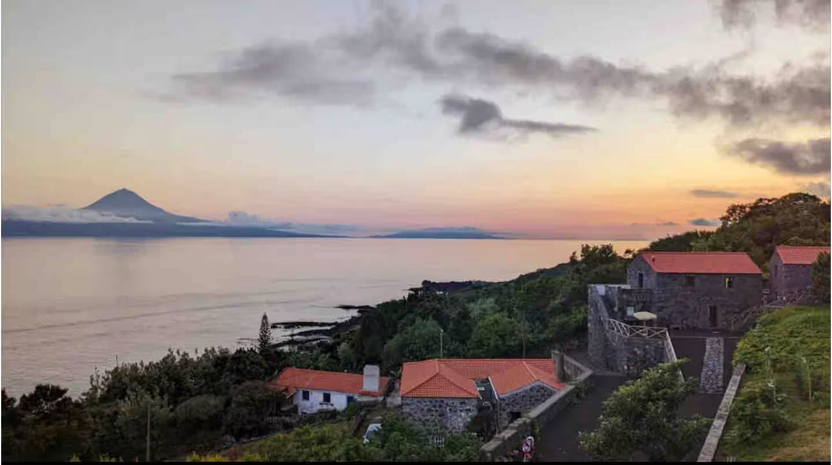 A coastal village with stone buildings, a clear view of the sea, and a distant mountain.