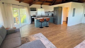 Ein großzügiger Wohnbereich mit Holzboden, einer Couch, einer Küche mit Kochinsel und einer Schiebetür zu einem Balkon.