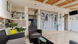 A covered outdoor seating area with wicker furniture, a tiled floor, and a wall with a large black and white mural.