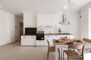 A modern kitchen with white cabinetry, a built-in oven, and a dining area with a wooden table and chairs. - Dimora Fico d'India by BarbarHouse (Lecce)