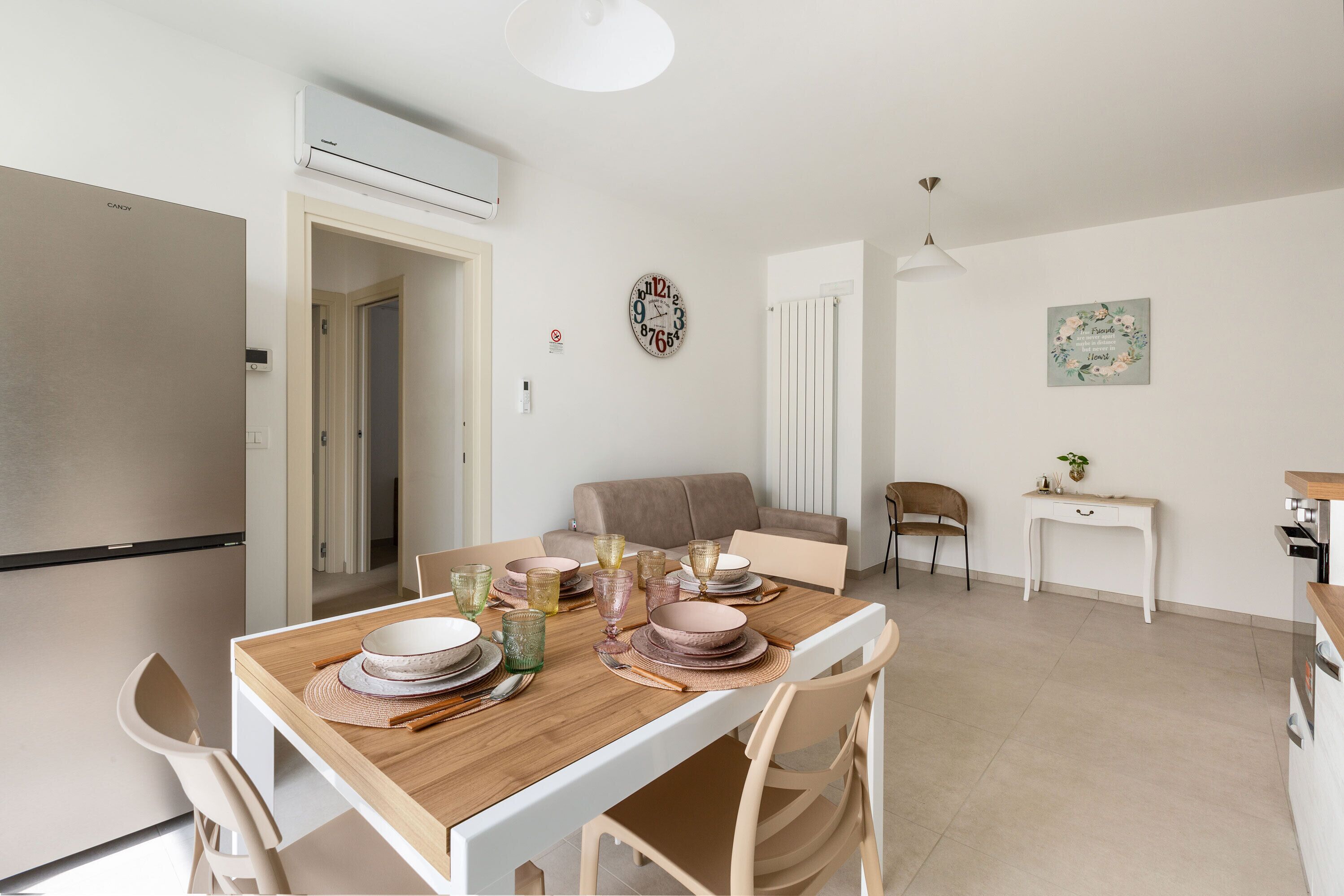 A modern kitchen with a built-in refrigerator, a dining area with a wooden table set for four, and a living area with a sofa and a small side table.