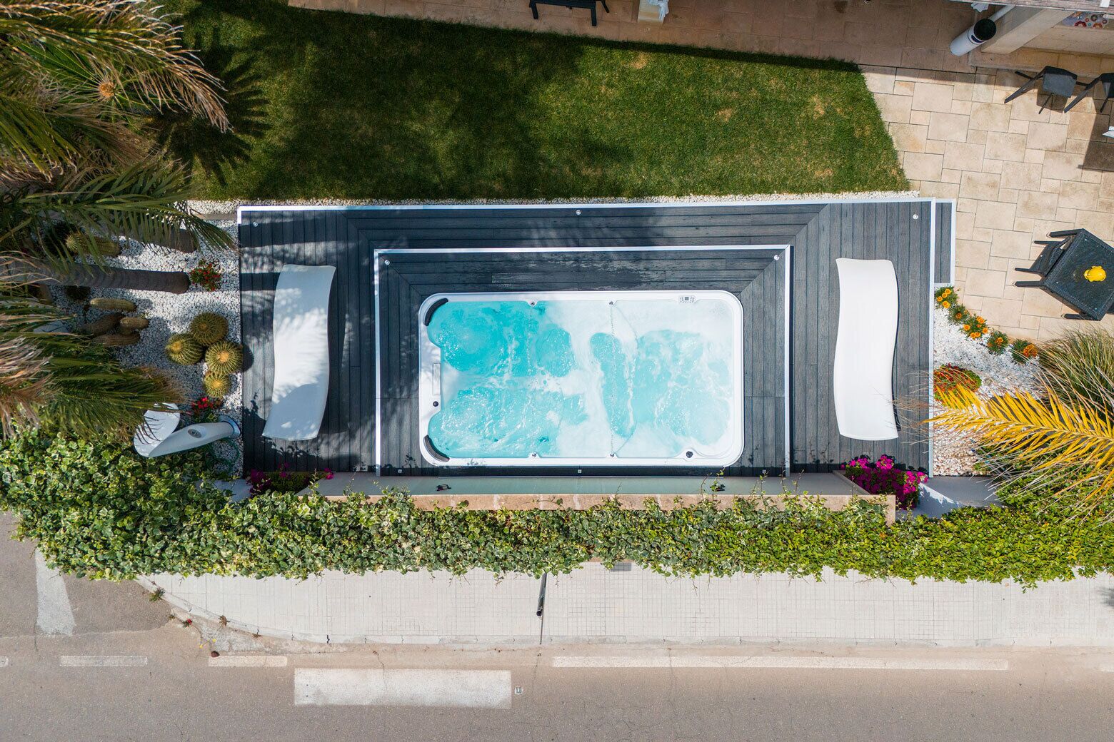 Un bain à remous extérieur, entouré d’un jardin où poussent différentes espèces de plantes, et bordé d’une zone dallée.