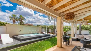 A covered outdoor area with a hot tub, seating, and a view of the sky.