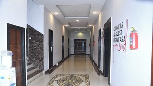 A hotel corridor with a marble wall, a patterned carpet, and a fire extinguisher on the wall.