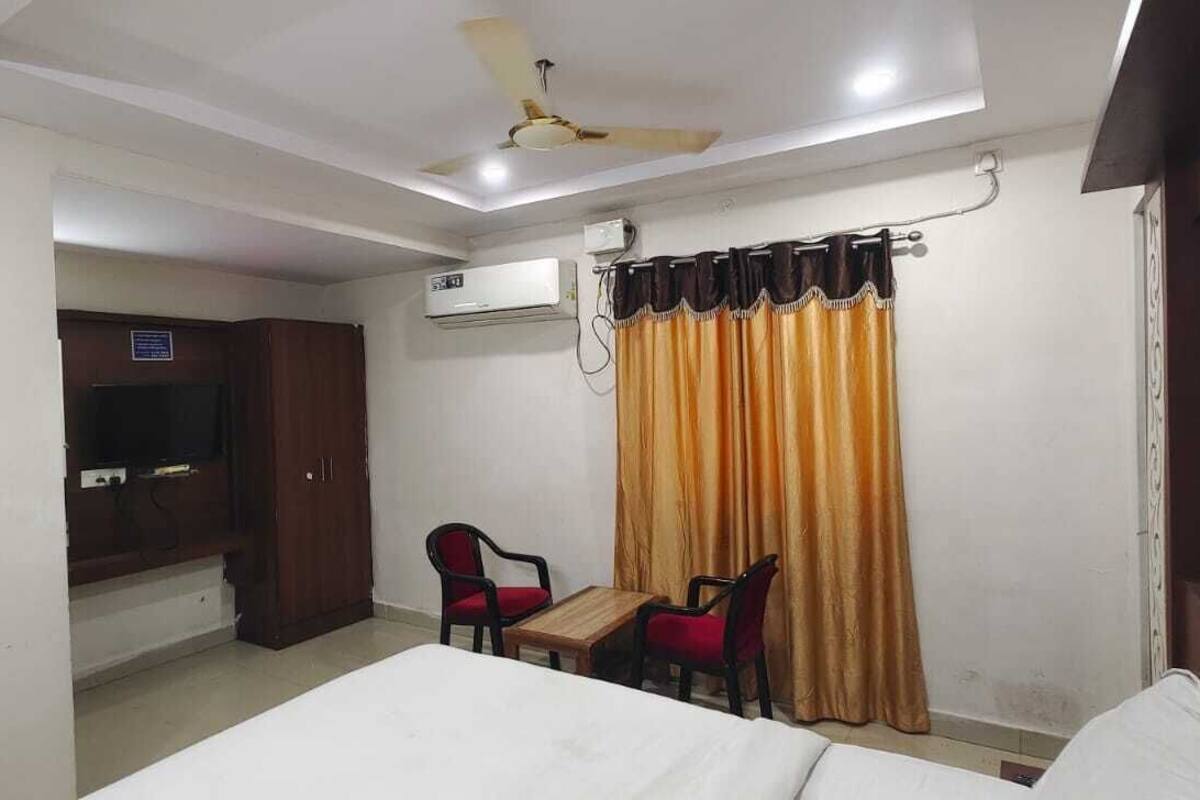 Habitación de hotel con cama, escritorio, dos sillas, televisor, unidad de aire acondicionado y cortina.