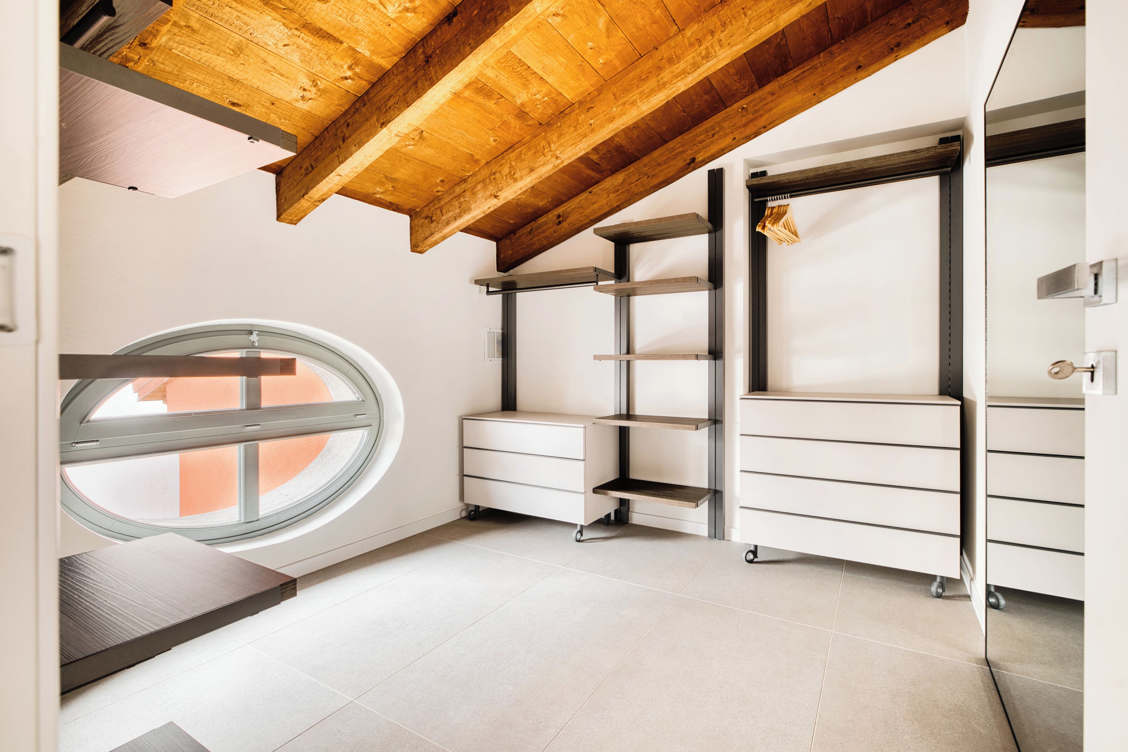 A room with a skylight, wooden beams, white storage units, and a view through the window.