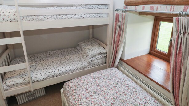 A bunk bed room with a window, a wooden headboard, and a small window seat. - The Gallops (Barry)