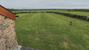A grassy field with a stone wall and a building with a sloped roof. - The Gallops (Barry)