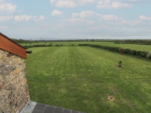 A grassy field with a stone wall and a building with a sloped roof. - The Gallops (Barry)