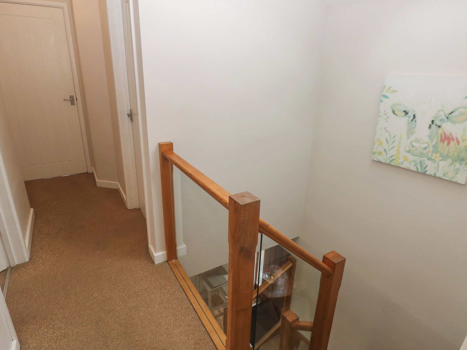 A hallway with a wooden handrail, carpeted floor, and a door at the end.