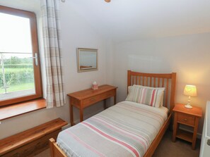 A bedroom with a bed, a bedside table, a nightstand, a window with curtains, a mirror, and a lamp. - The Gallops (Barry)