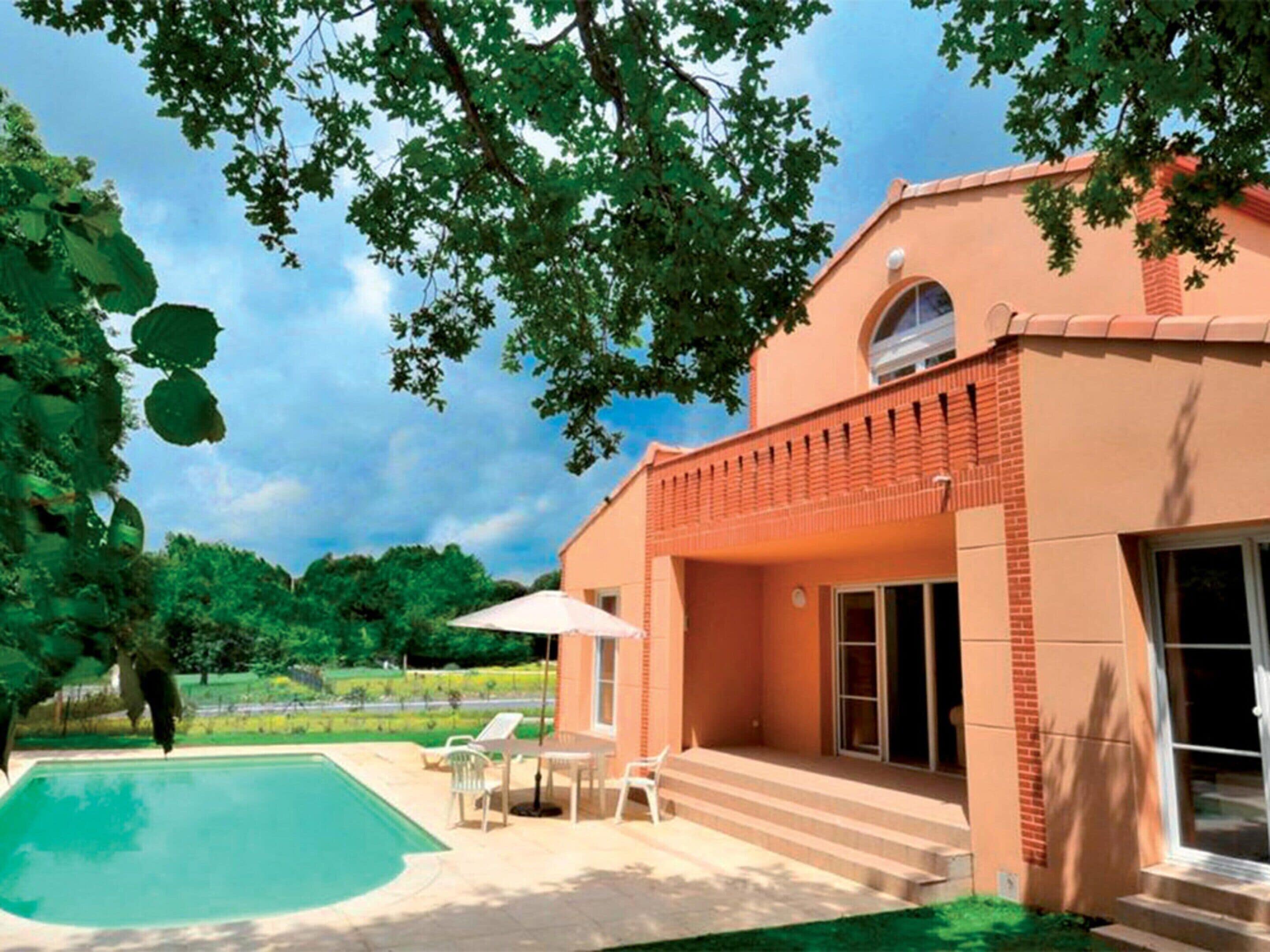 A house with a swimming pool, a patio with chairs, and a view of the surrounding greenery.