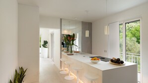 A modern kitchen with a central island, bar stools, a large window, and a view of greenery. - Villa Lunezia 6, Emma Villas (Aulla)