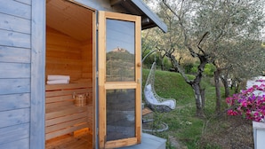 A wooden sauna with a glass door, a hanging chair, and a view of a hill. - Villa Lunezia 6, Emma Villas (Aulla)