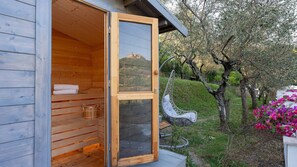 Una sauna in legno con porta in vetro, una sedia a dondolo e vista su una collina.