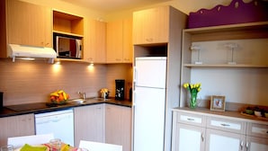 Une cuisine moderne avec des meubles en bois, un four à micro-ondes encastré, un réfrigérateur et un coin repas avec une table dressée pour deux personnes.