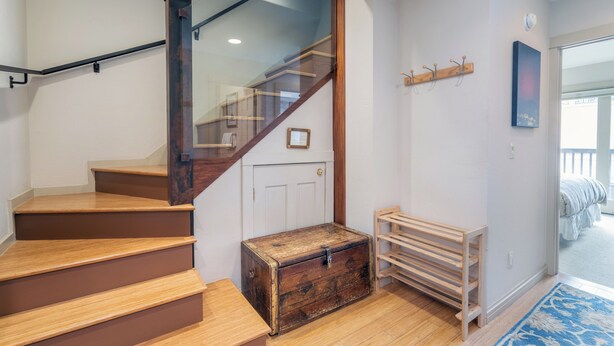 A staircase with wooden steps and glass railings, a wooden chest, a coat rack, and a bed in the adjacent room. - Luxury 3-Bedroom, Heart of Telluride, Mtn Views, 3 min walk to Gondola & Trails (Telluride)
