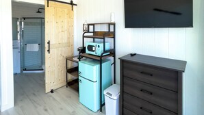 Quarto compacto com porta de celeiro deslizante, micro-ondas, pequena geladeira, cômoda escura e televisão na parede.