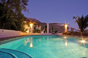 Ein Swimmingpool mit klaren, blauen Fliesen, umgeben von tropischen Pflanzen und einem Berg im Hintergrund.