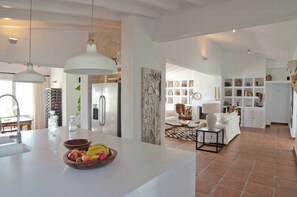 Eine moderne Küche mit Kochinsel, Essbereich mit Sofa und Couchtisch sowie ein Wohnzimmer mit Kamin.