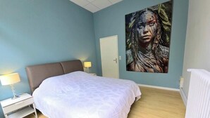 Une chambre à coucher avec un lit, une table de chevet, un tableau accroché au mur et une porte.