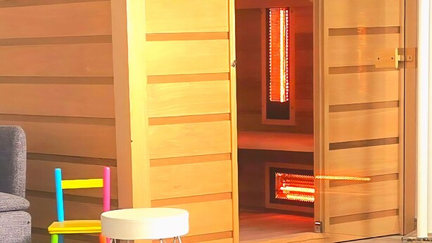 Un sauna en bois doté d’une porte coulissante, d’une petite table et de chaises colorées.