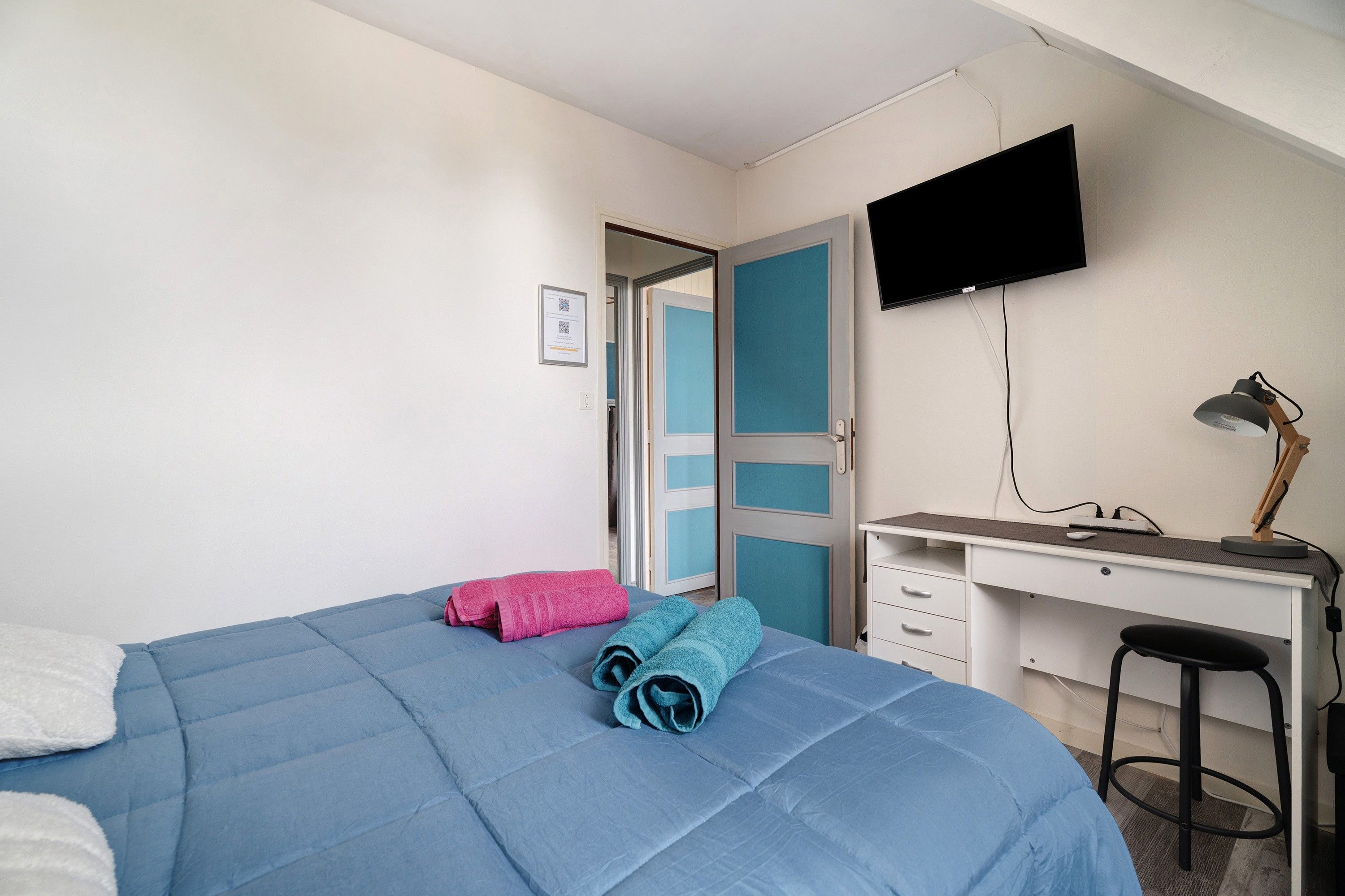 Een hotelkamer met een bed, een bureau, een stoel, een televisie en een deur.