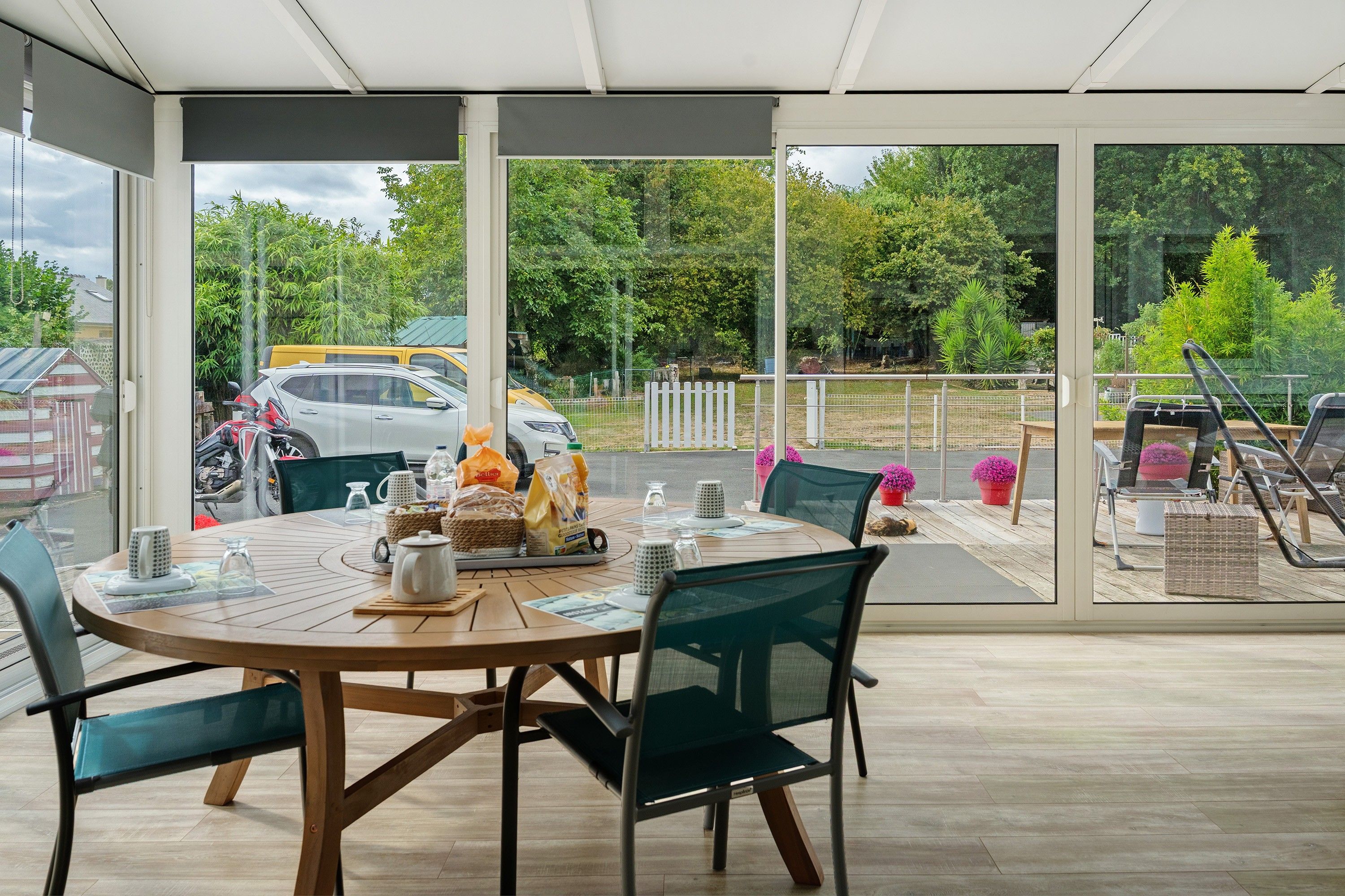 Un espace extérieur abrité, aménagé pour les repas, avec une table pour deux, des chaises et une vue sur la rue et la verdure environnante.