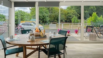Un espace extérieur abrité, aménagé pour les repas, avec une table pour deux, des chaises et une vue sur la rue et la verdure environnante.
