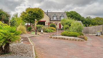 A house with a gravel driveway, surrounded by various plants and a statue.