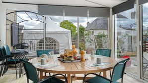 Un área de comedor exterior moderna con una mesa redonda, sillas y un cerramiento de vidrio.