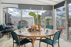 A modern outdoor dining area with a round table, chairs, and a glass enclosure. - Between Saint-Malo, Dinan, Mont-Saint-Michel: Bed & Breakfast - 3 Bedrooms (Miniac-Morvan)