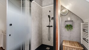 Un baño moderno con cabina de ducha de vidrio, un toallero blanco y un taburete de madera pequeño.